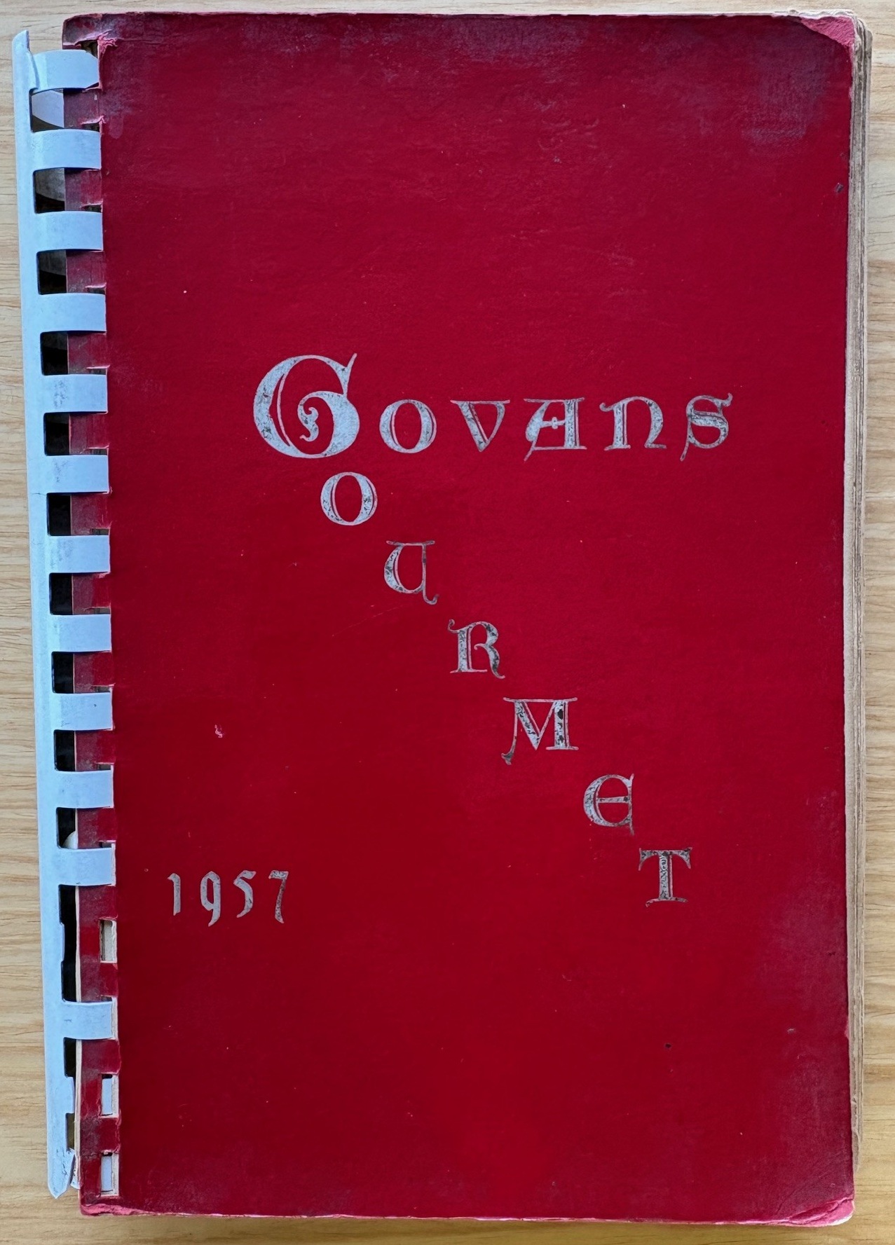 Copy of the book Govans Gourmet, with a red cover and white plastic spiral binding and silver text
