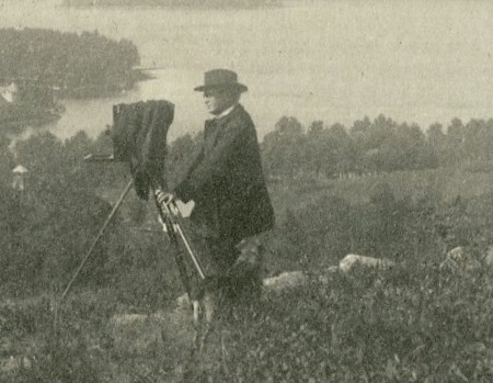 Photograph of Father Griffin standing with a camera in a field