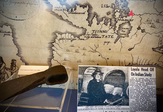 A photo of exhibit materials including a historic map, an axe head, and a newspaper article titled 'Loyola Head Off On Indian Study'