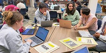 Students and professor working on laptops and conversing